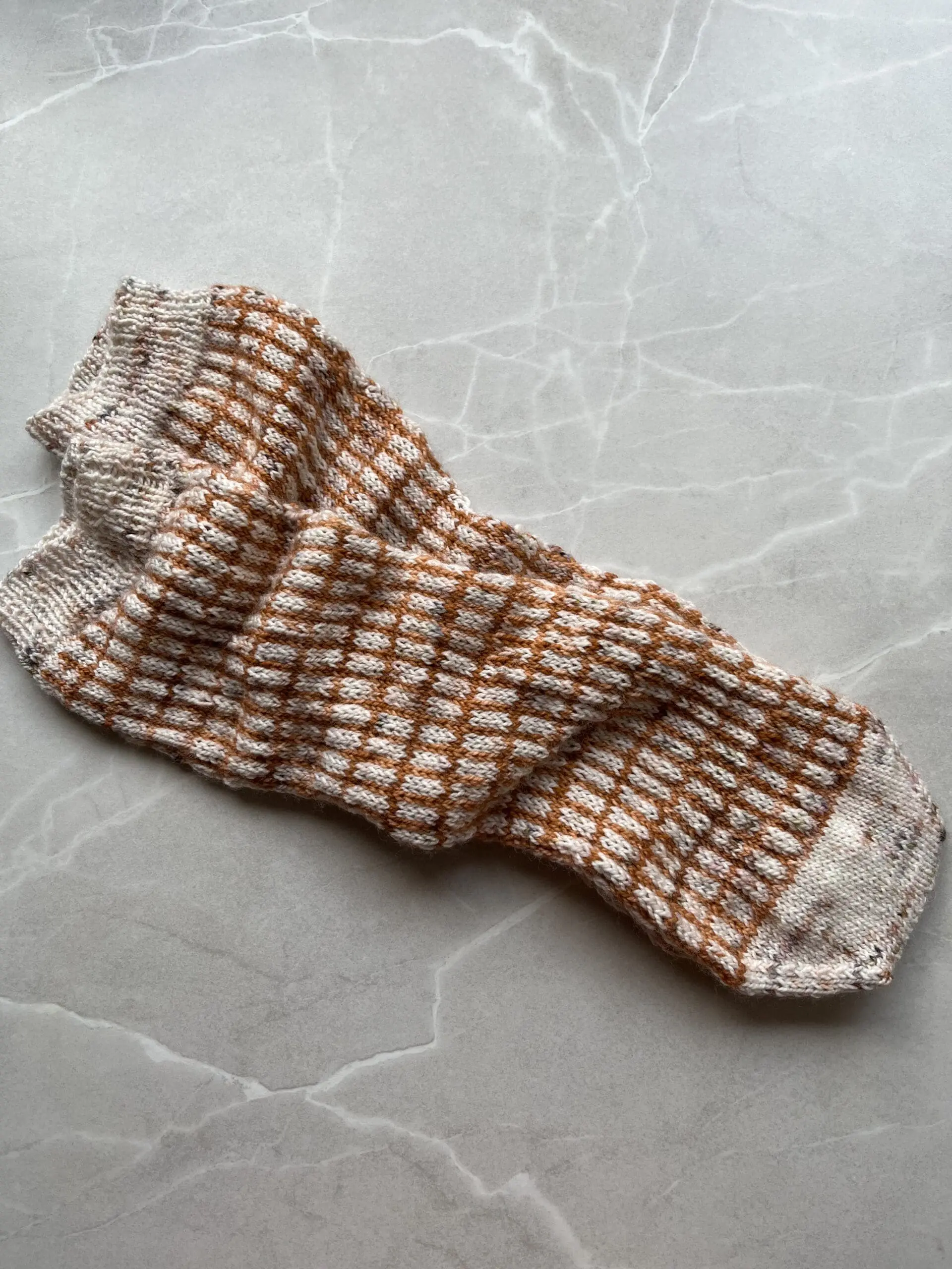 Cottage socks af Mette Lundstad strikket i brun og hvid der ligger på et bord