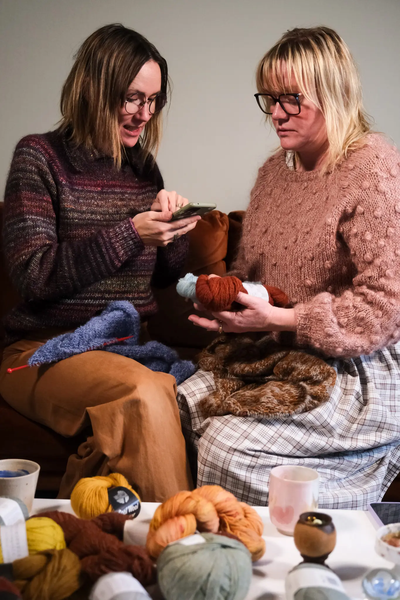 Mette og Helena sidder på en sofa med meget garn