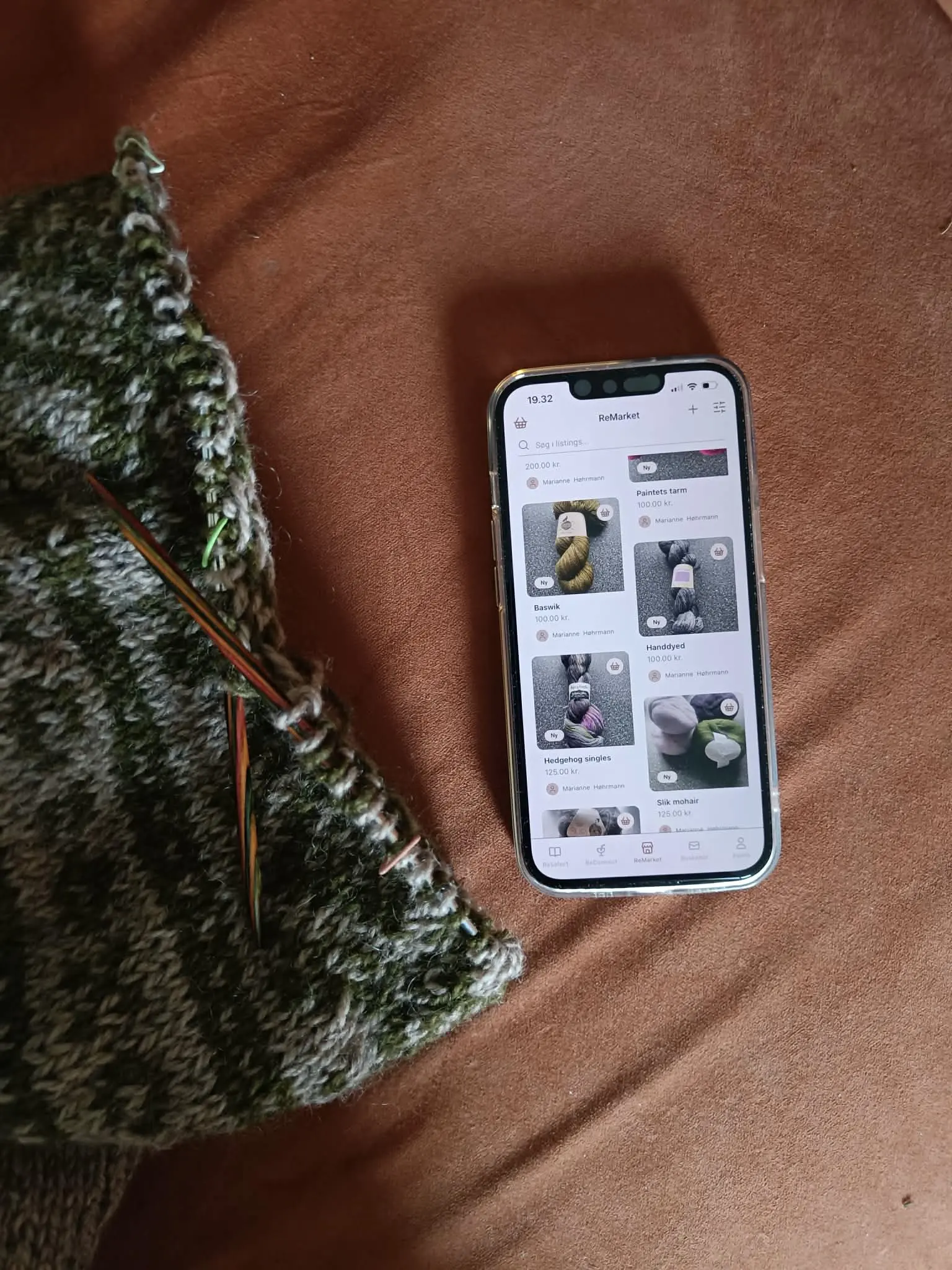 En telefon ligger med appen åbent og et strikketøj ved siden af