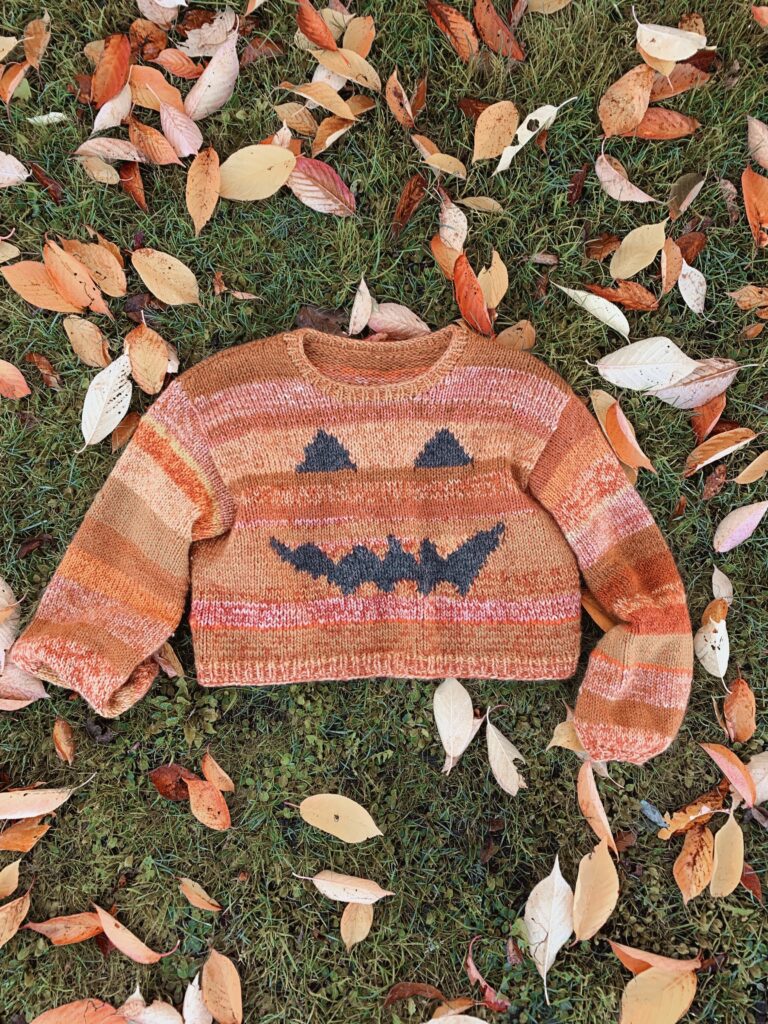 Halloween sweateren af Mette Lundstad strikket i garnrester der ligger på en græsplæne
